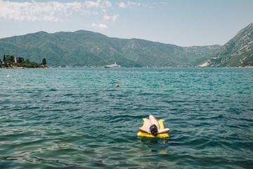 young adult woman on yellow mattress in blue sea water.