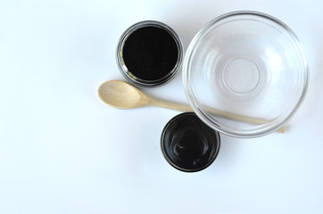 Top view of cosmetic black powdered activated charcoal and beauty face mask mixture in a bowl with copy space on white. 
