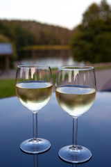 Romantic couple of glasses of wine on a table with reflections and view of nature on background