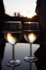 Romantic couple of glasses of wine on a table with reflections and sunset in the background
