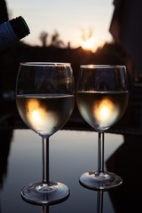 Romantic couple of glasses of wine on a table with reflections and sunset in the background