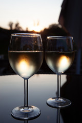 Romantic couple of glasses of wine on a table with reflections and sunset in the background