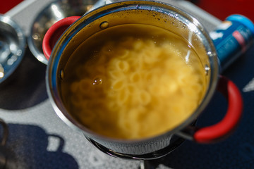 Cooking on a portable gas stove, on a folding table in the background of camping in the woods. Spaghetti in a pot on a gas burner (camp stove).