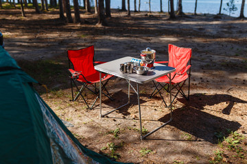 Family vacation, travel concept on wheels, a road trip, a table and chairs, a tent and a SUV with the back door open on site. Folding table and chairs with gas stove in the camping in the forest.