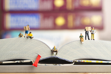 Close up of miniature figures of a group of people read book and newspaper.