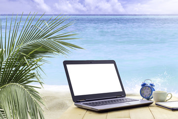 Laptop computer and hot coffee and clock and note on wooden table at the beach in summer