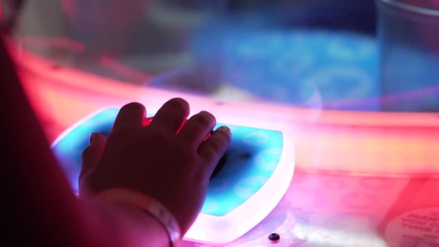 A slo-motion shot of a hand resting on the big red button of an arcade game.