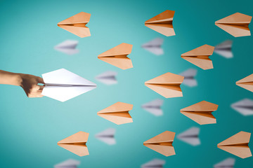 Hand launches a paper plane to towards other aircrafts on blue background