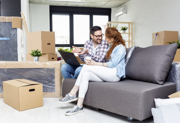 Young couple in new home with notebook sitting on sofa and planning with unpacked boxes in background