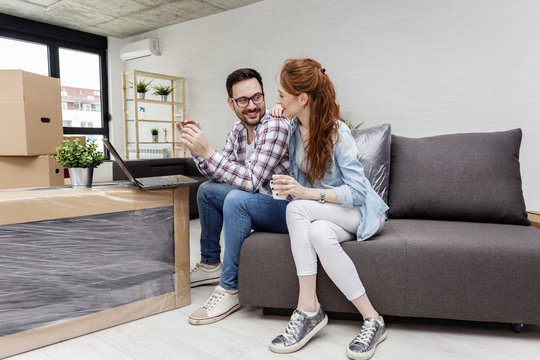 Young couple in new home with notebook sitting on sofa and planning with unpacked boxes in background
