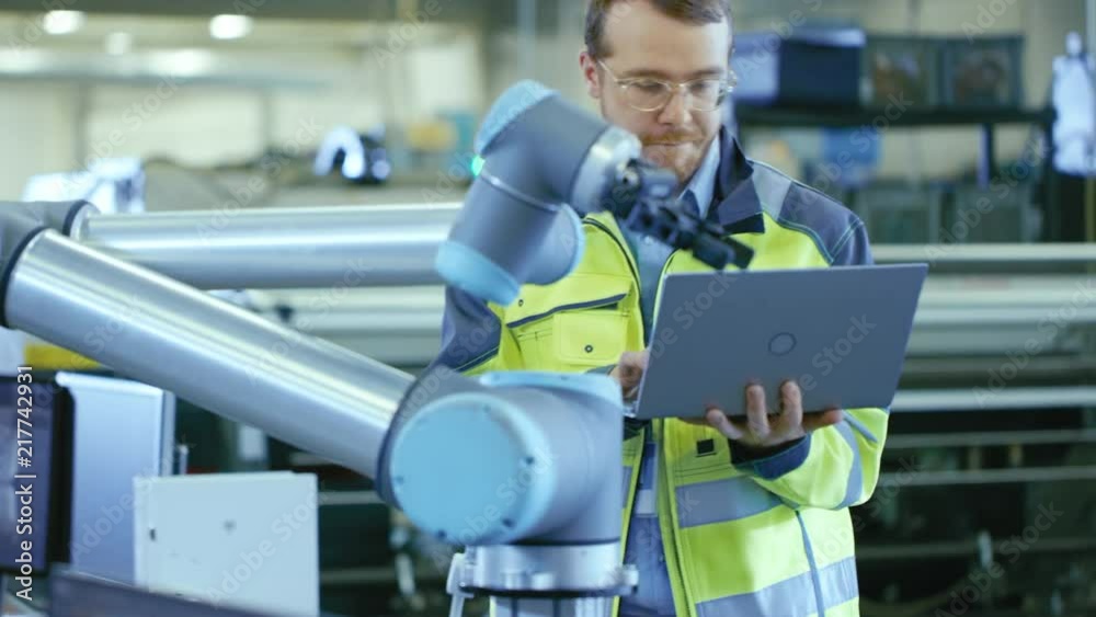 Poster At the Factory: Automation Engineer Uses Laptop for Programming Robotic Arm. New Era in Automatic Manufacturing Industry.