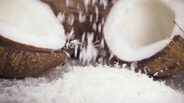 Slow motion coconut shavings abundantly pours on the table near the half of the coconut