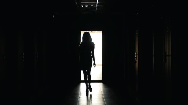 Beautiful woman walks in a dark corridor, silhouette