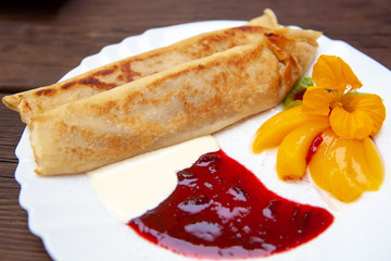 White plate with pancakes, with jam, cream, fruit and flower on a wooden table