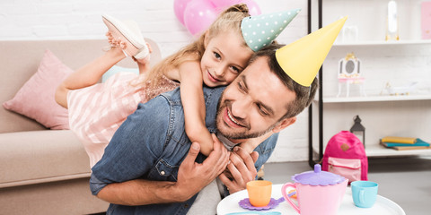 father and daughter in cone hats piggybacking while playing tea party at home