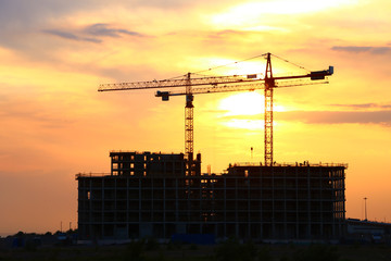 construction with tower cranes on a bright sunset background