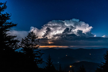 A huge thunderstorm with active lightning lighting up the clouds is seen from the high peak of...