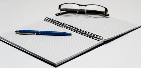 Notebook and glasses and red pen on table. White background