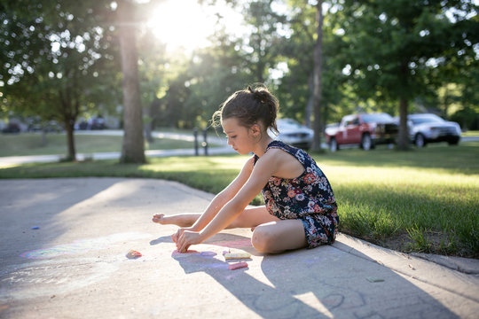 Side view of girl drawing with chalks on footpath in yard