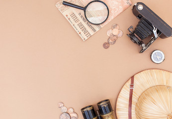top view on items for travel, recreation and adventure: map, vintage paper and coins, magnifying glass, compass, clock and safari hat on a beige background with space for text as a frame. flat lay