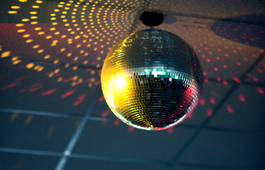 Sparkling silver disco ball with yellow and pink sparkles on the ceiling in the night club