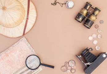 top view on items for travel, recreation and adventure: map, binoculars, straw hat, vintage paper and coins, magnifying glass, clock, compass and camera on a beige background as a frame. flat lay
