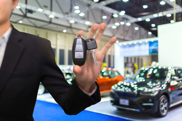 Salesman or dealer offering car keys to new owner in showroom, buy or rent concept.