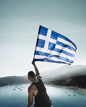 Rear view of man waving Greek flag while standing over sea against sky