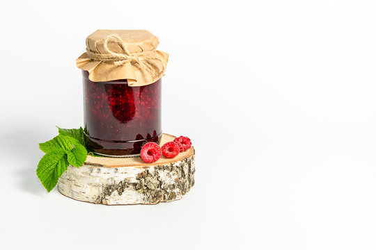 Jar with jam of raspberries wrapped in wrapping paper, stands on a birch stump on white background, on white background