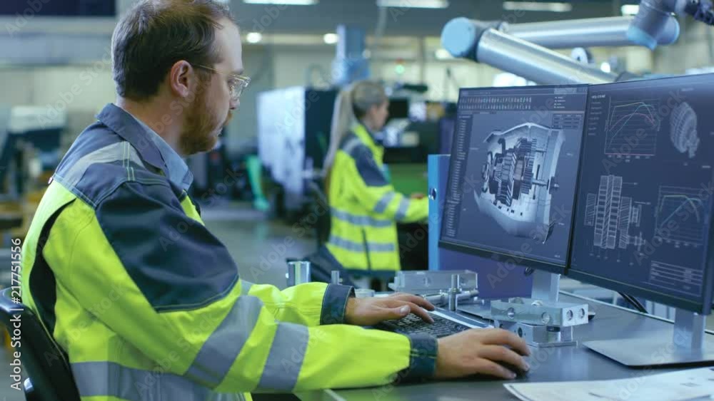 Poster At the Factory: Mechanical Engineer Works on Computer, Designs in CAD 3D Model of the Engine. In the Background Factory Workers and Manufacturing Process. Shot on RED EPIC-W 8K Helium Cinema Camera.