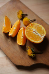 Orange cut into pieces lies on a wooden cutting Board. Around the orange slices are the flowers of the dandelion.
