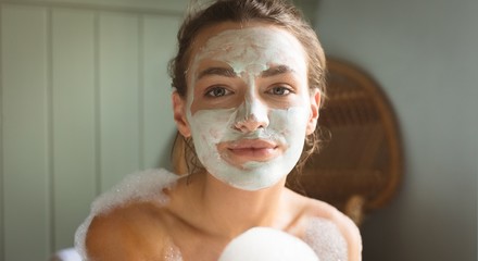 Woman with facial mask on face taking bath in bathroom
