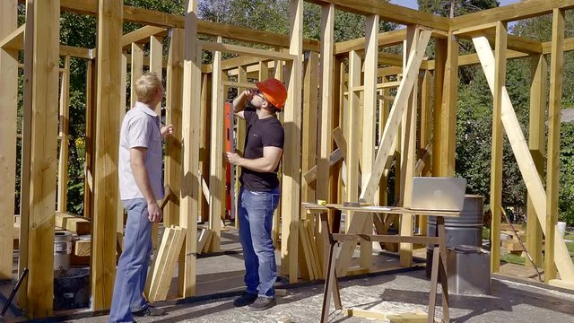 developer and customer are standing inside building house between wooden beams in sunny day, owner is reading papers