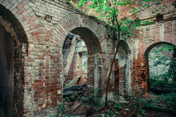 Old ruins of a medieval abandoned ruined red brick castle with arches overgrown with trees and plants
