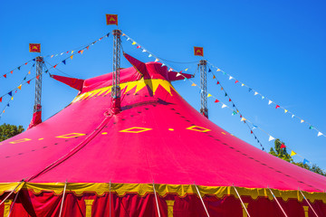 Circus tent detail. Red circus tent in green built in a green field against a blue sky.