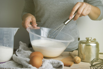 Close-up young woman's hands holding whisk and bowl while making pie, cake. Female cooking dough for pie on wooden table. Preparring dessert.