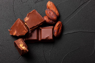 Сhocolate pieces and cocoa powder on marble. The chunks of chocolate over dark background