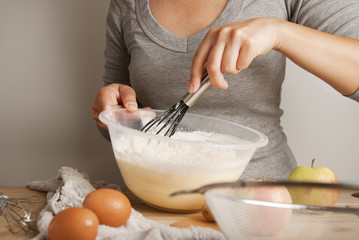 Close-up young woman's hands pourring milk, making pie, cake. Female cooking dough for pie on wooden table. Preparring dessert.