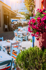 Traditional Greek vivid colored tavern with purple flowers on the narrow Mediterranean street on hot summer day