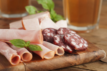 Variety of meat snacks to beer: ham, rolled meat, with fresh basil and glass beer over dark wooden background. Close up.