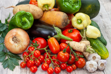 Colourful variety of fresh home grown vegetables from an organic garden on a wooden surface. Tomato, green and yellow bell peppers, carrot, parsley, onion, garlic, potato, eggplant and zucchini.