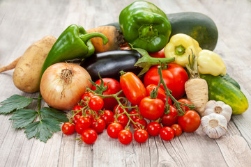 Colourful variety of fresh home grown vegetables from an organic garden on a wooden surface. Tomato, green and yellow bell peppers, carrot, parsley, onion, garlic, potato, eggplant and zucchini.