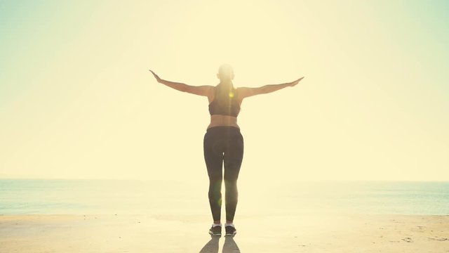 Beautiful sportive girl training at sunrise over seaside. Woman doing yoga against the sea and sun.