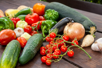 Colourful variety of fresh home grown vegetables from an organic garden on a wooden surface. Tomato, green and yellow bell peppers, carrot, parsley, onion, garlic, potato, eggplant and zucchini.