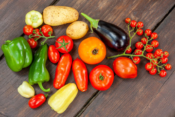 Colourful variety of fresh home grown vegetables from an organic garden on a wooden surface. Tomato, green and yellow bell peppers, carrot, parsley, onion, garlic, potato, eggplant and zucchini.