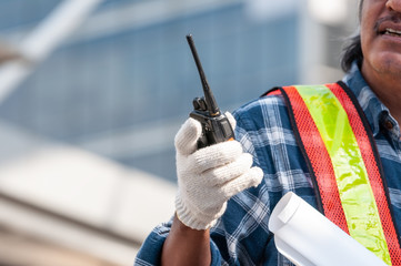Unidentified senior Asian civil engineer wearing white glove holding walkie talkie radio and...