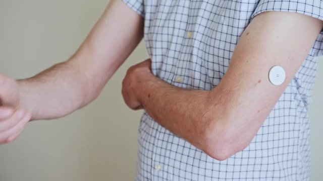 A man brings to the hand the reading device to the sensor for measuring glucose