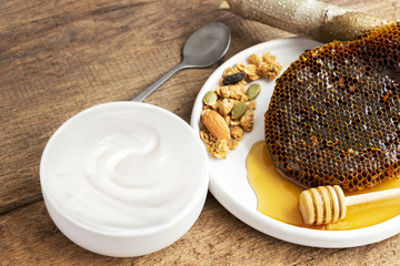 Healthy flavored yogurt in ceramic bowl with honeycomb and honey on the wooden background with copy space for your text.