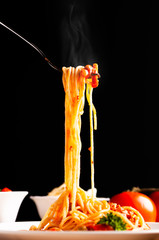 Hot spaghetti with tomato sauce in white plate,  food stylish action with black background, pull spaghetti up with fork.