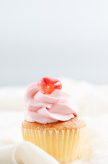 Single butter cup cake with strawberry cream and red cherry on table and soft cloth with blur background, bakery dessert for party.